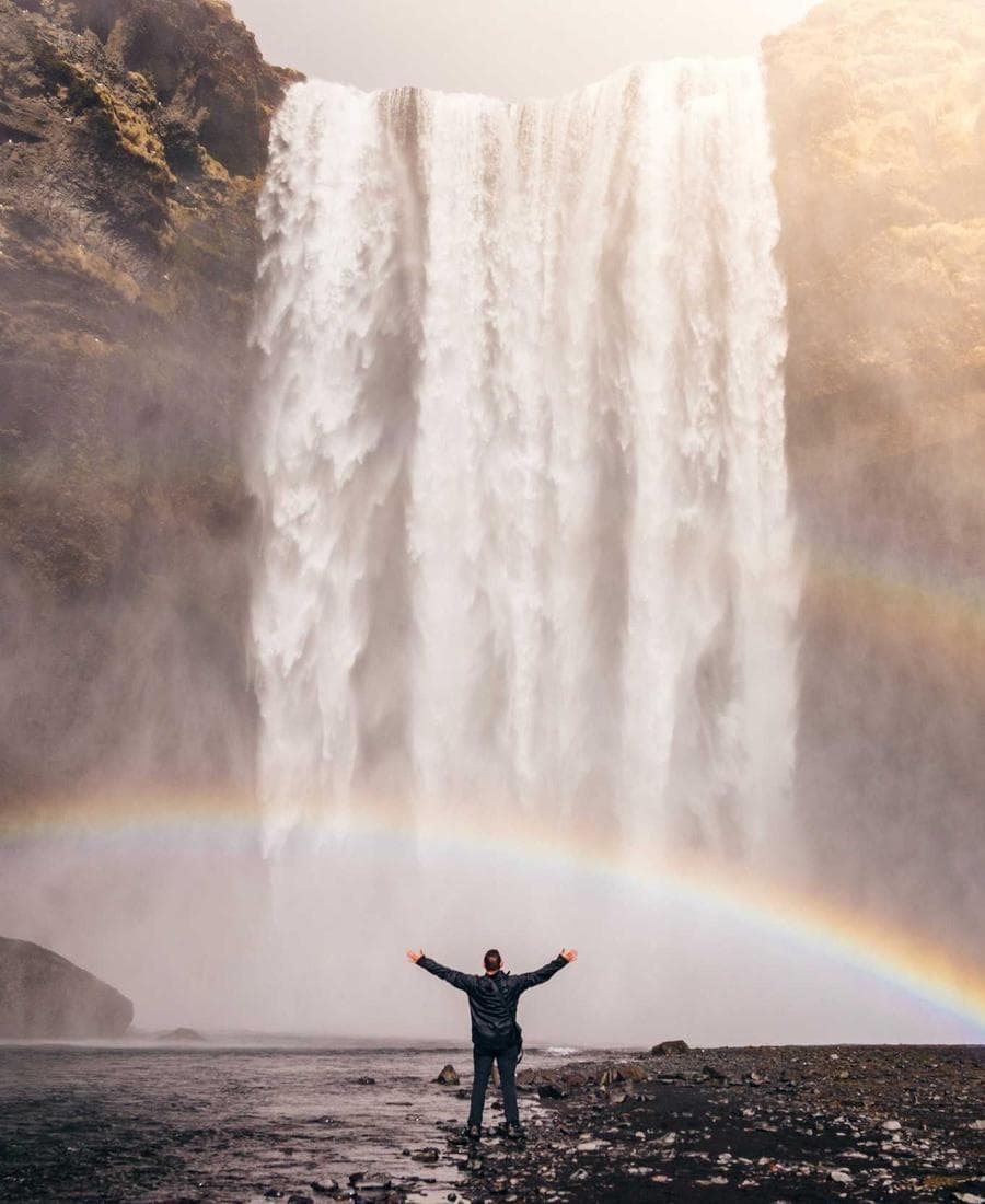 A person under a waterfall with a rainbow
